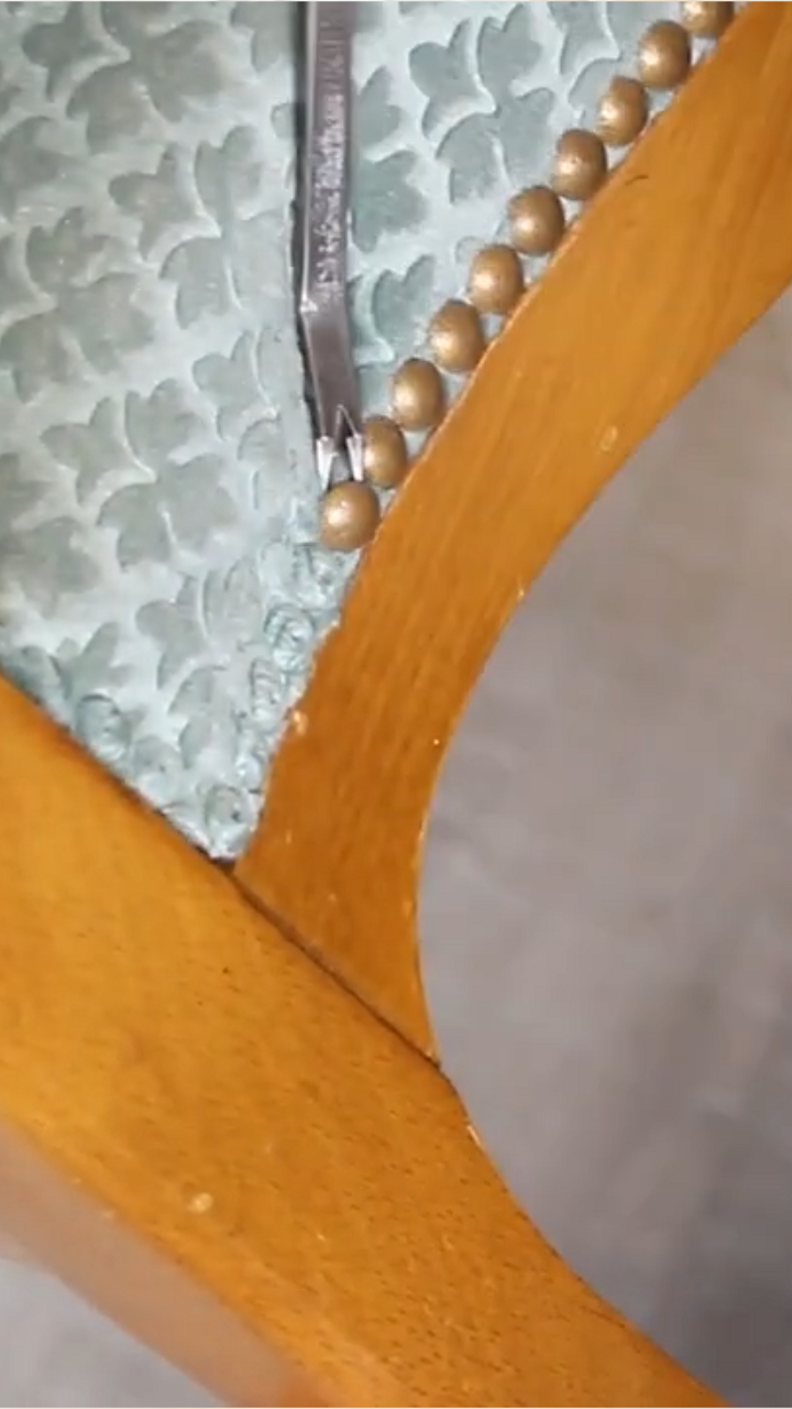 Gros plan sur un fauteuil en cours de restauration, avec des clous décoratifs retirés un par un. Explication sur pourquoi on ne réutilise pas les vieux clous
